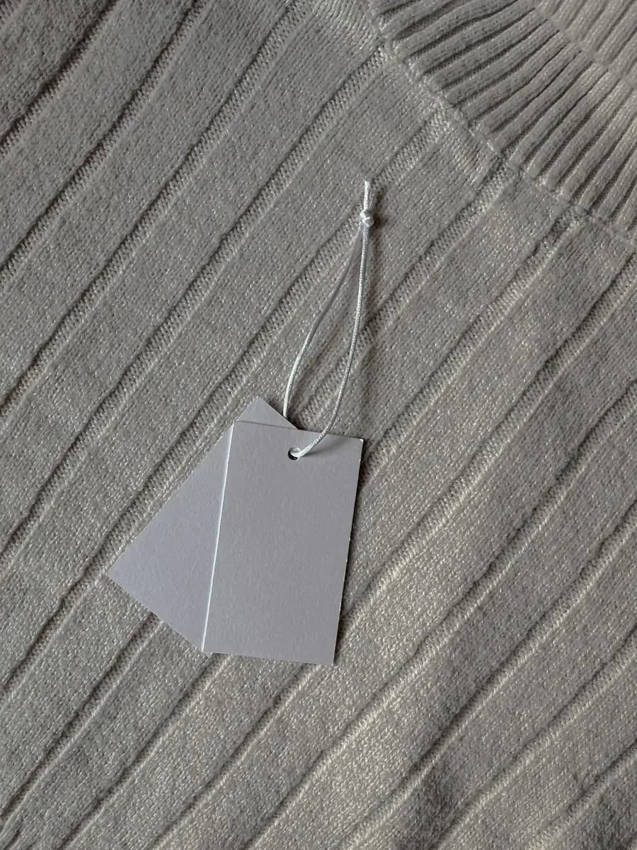 Two blank hangtags on a string resting on ribbed knitwear