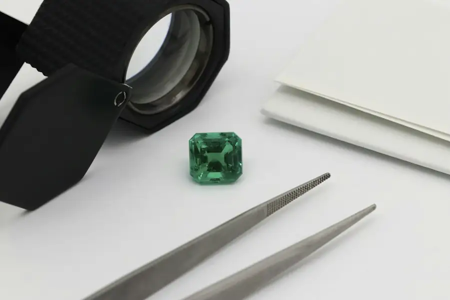 Green emerald beside a loupe and tweezers