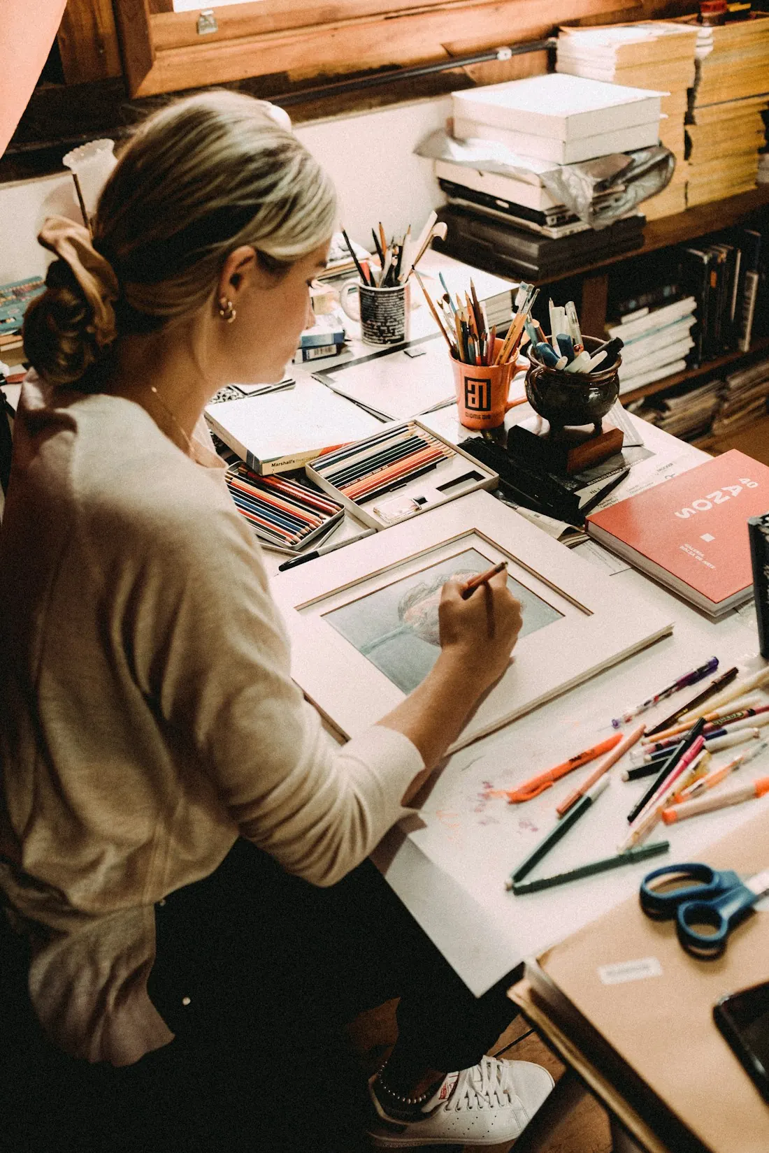 Designer drawing at a desk covered in pencils and sketches