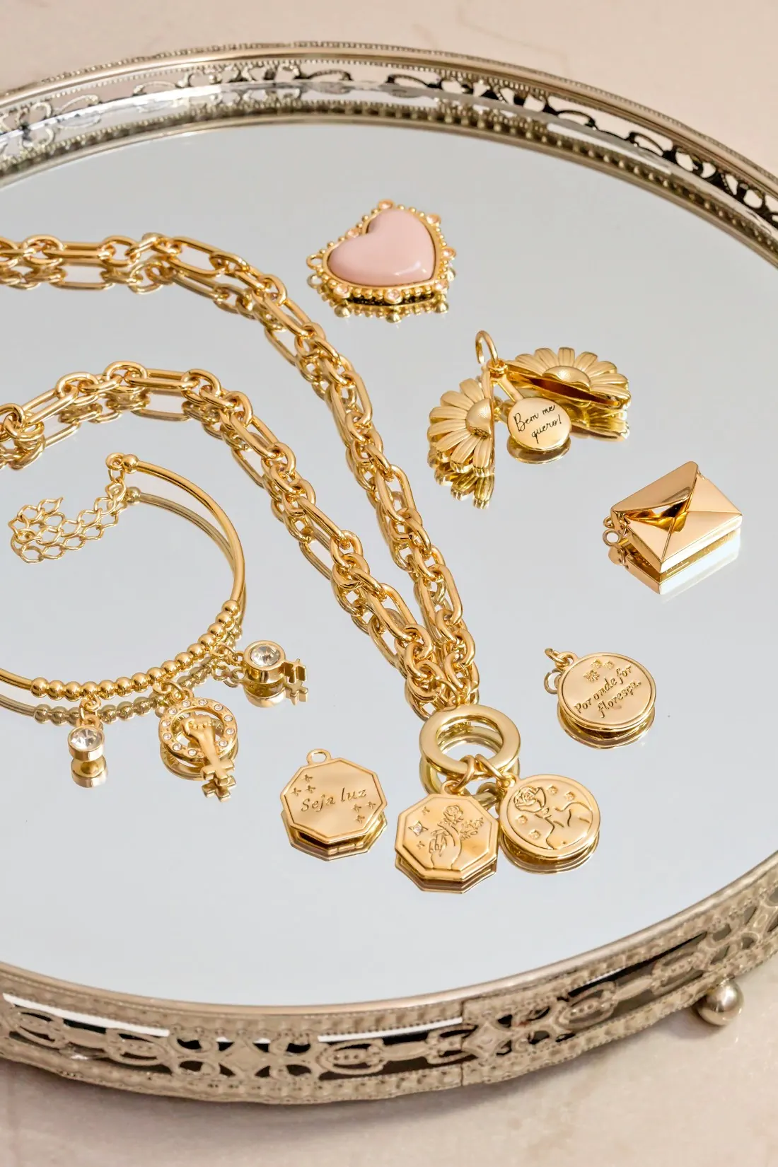 Gold chains, charms and bracelets on a mirrored tray