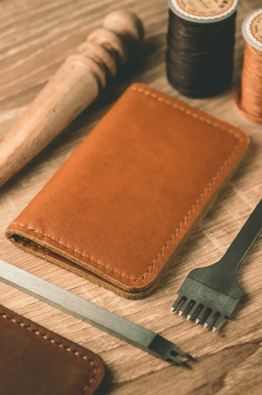 Leather wallet, thread and stitching tools on a wooden table