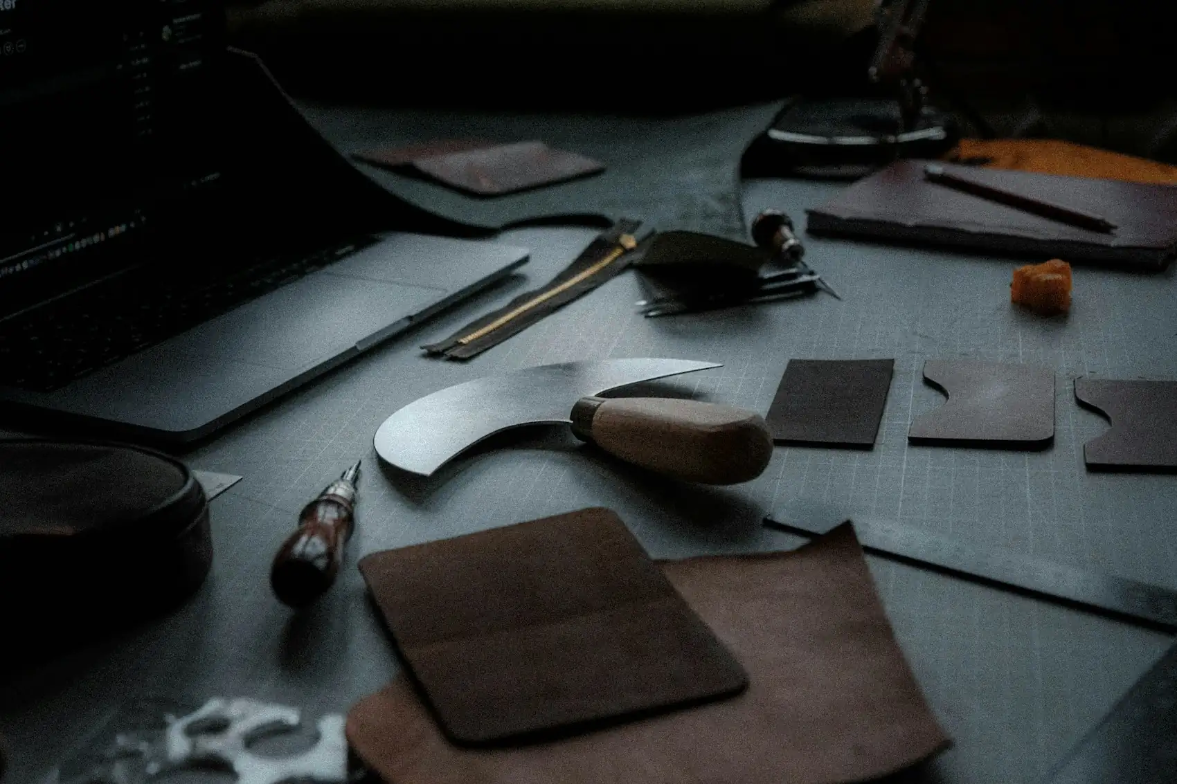 Leather pieces, a skiving knife and tools laid out on a dark workbench