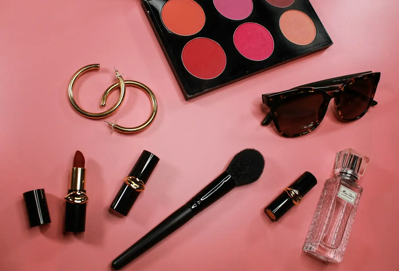 Flat lay of sample products: lipsticks, hoop earrings, sunglasses and a perfume bottle