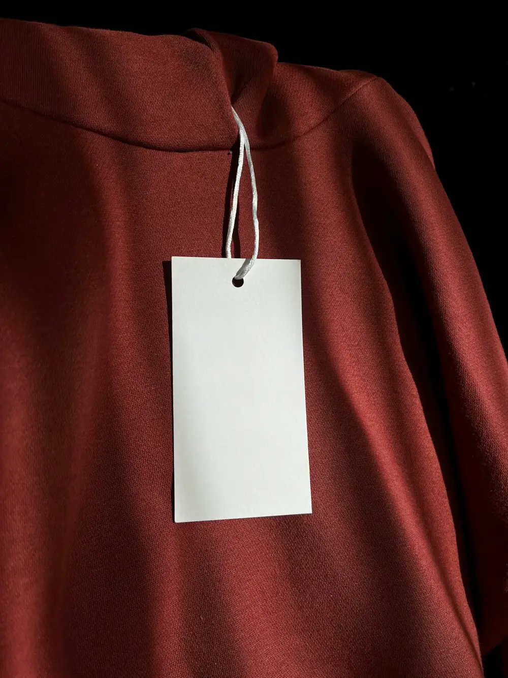 Blank hangtag on a rust sweatshirt, ready for a brand name