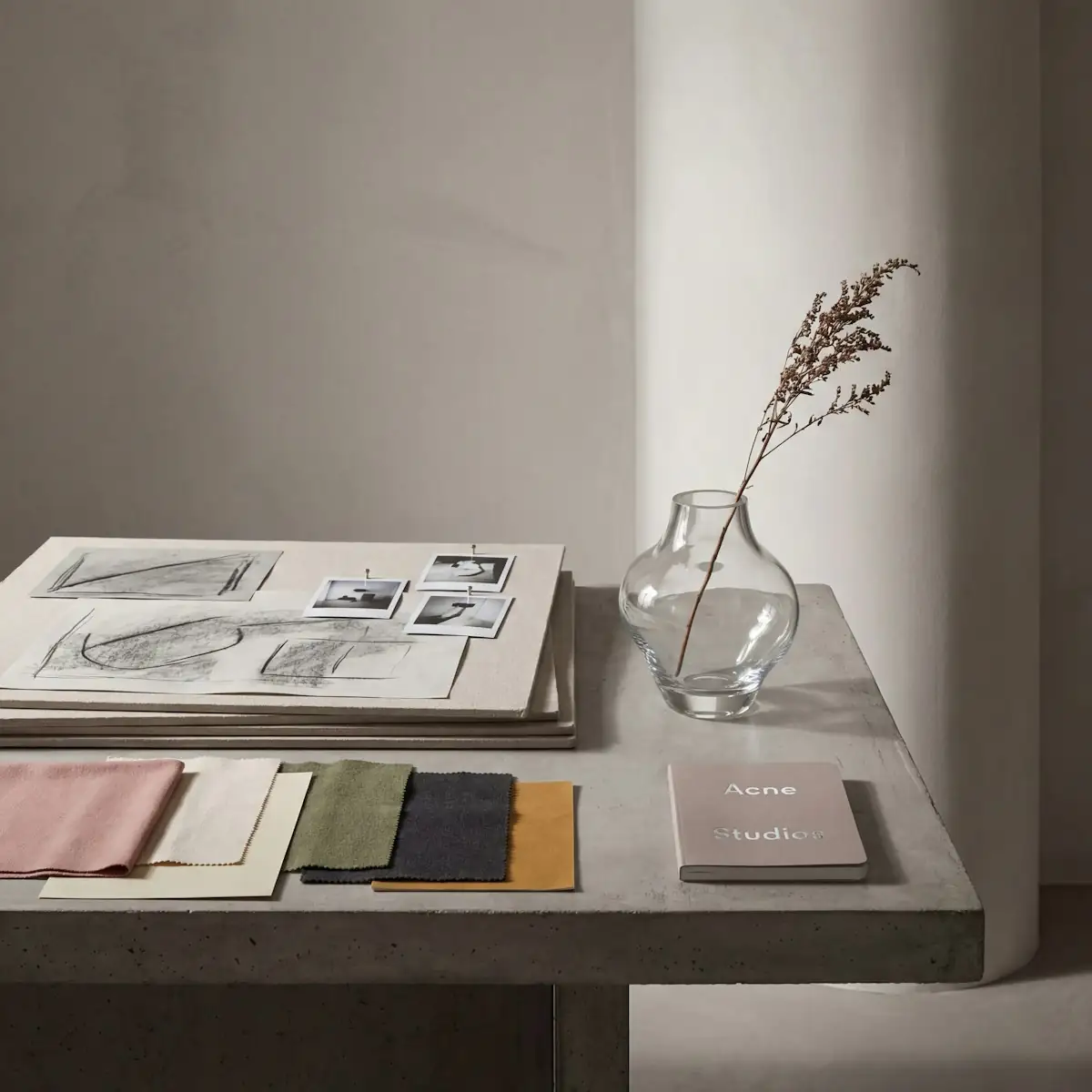 A designer desk with an open sketchbook, fabric swatches in muted colors and a glass vase