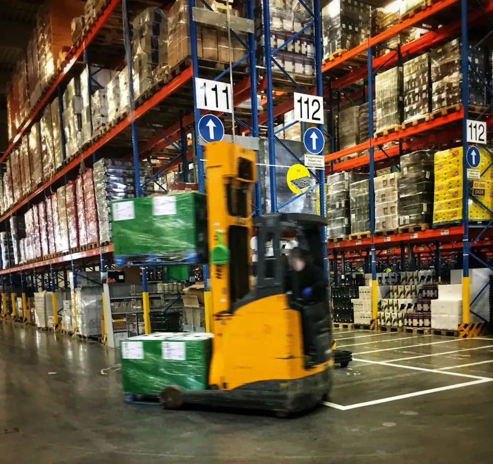 Forklift moving pallets between tall warehouse racks