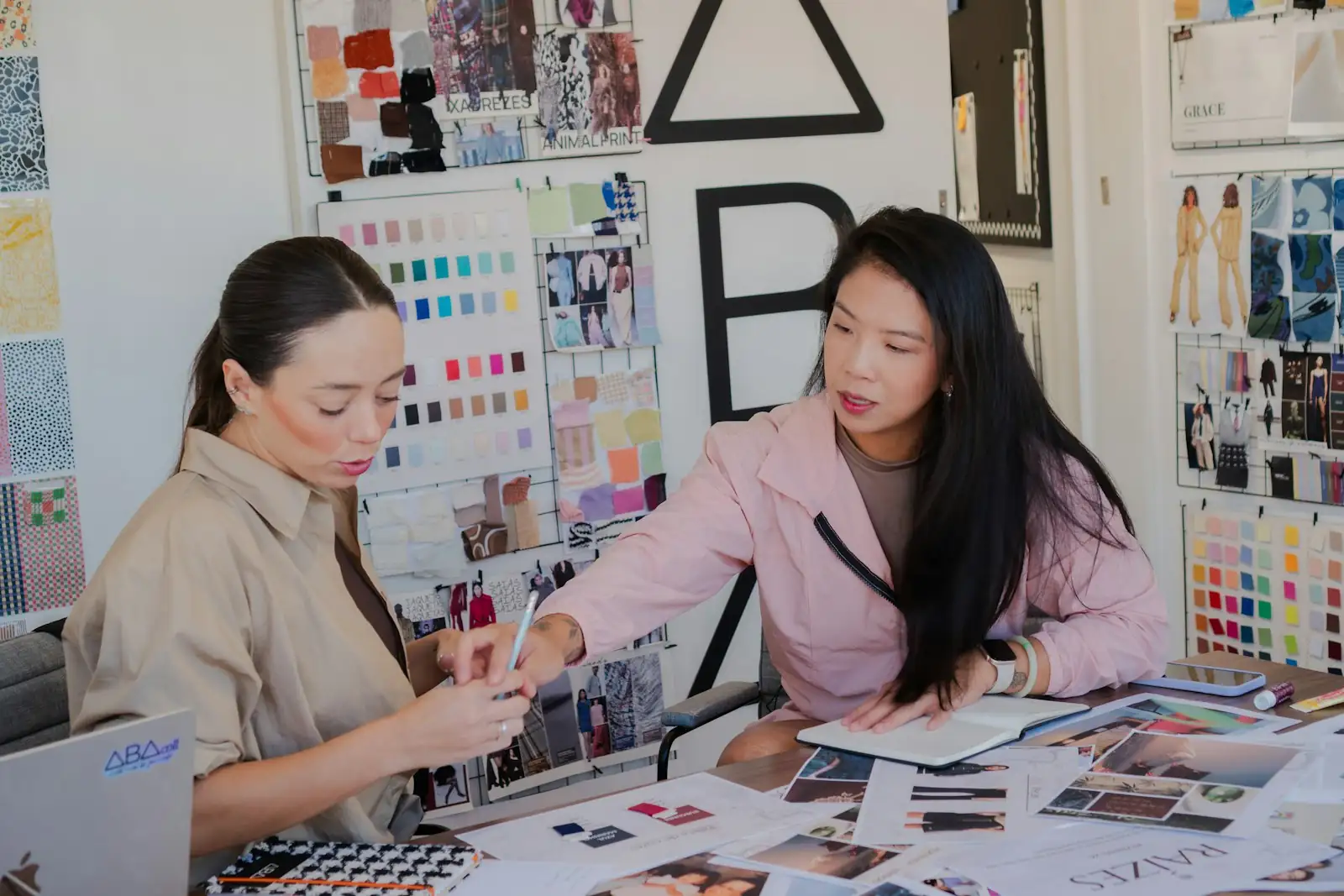 Two women at a desk reviewing fabric swatches, color charts and design printouts together